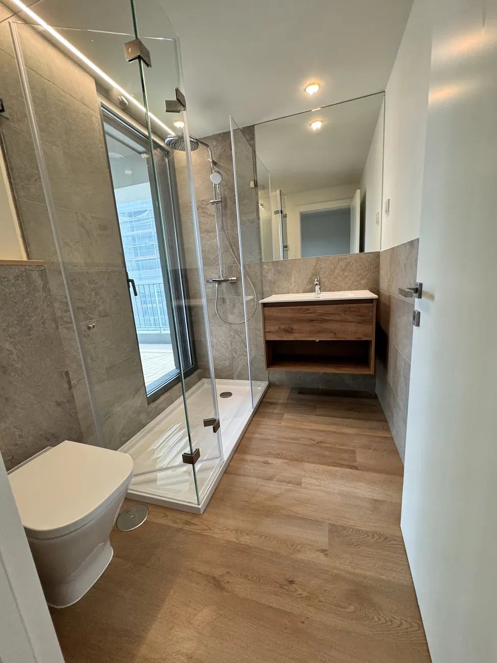 Casa de banho com pavimento vinílico SPC click em carvalho instalado pela Revest, com base de duche e resguardo de vidro